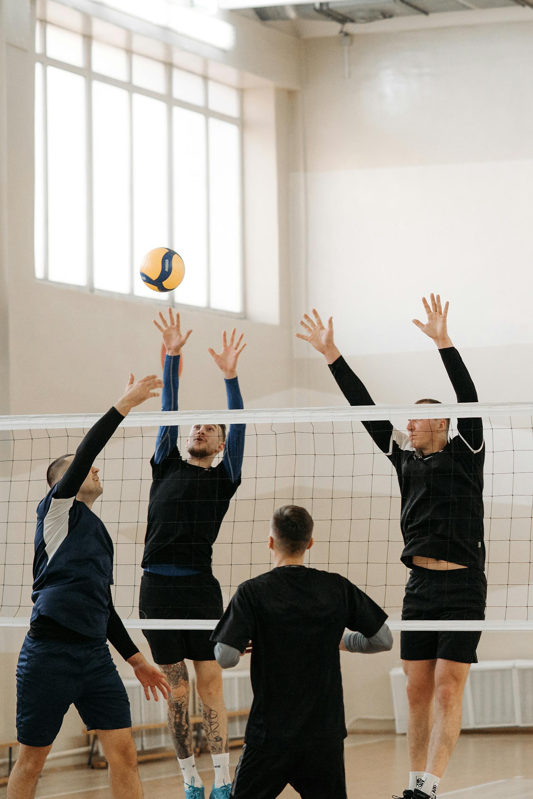 Dynamic indoor volleyball match with athletes jumping to block a ball over the net.